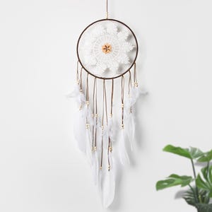 May include: White dream catcher with a brown wooden ring and white feathers. The dream catcher has a white crocheted design in the center.