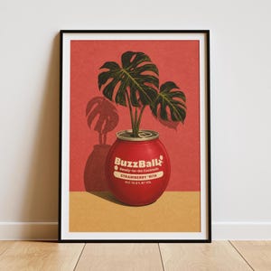 Puede incluir: Una impresión artística enmarcada que muestra un recipiente de cóctel rojo BuzzBallz Strawberry 'Rita usado como maceta para una planta monstera verde. El fondo es rojo sólido con una base color canela, y el texto dice BuzzBallz Ready-to-Go Cocktails.