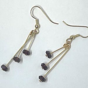 May include: A pair of gold earrings with three dangling strands each. Each strand has a dark brown, square-shaped bead.