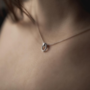 Puede incluir: Un collar de plata con un simple colgante circular.