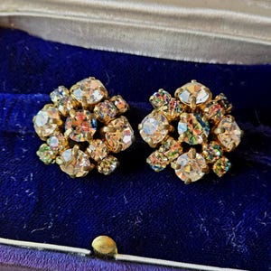 May include: A pair of vintage gold tone earrings with iridescent clear rhinestones. The earrings are in a flower shape and are in a small box with a label that reads "U. Visiano Gioielliere - Argentieri Via Cesare Battisti 3 TORINO".