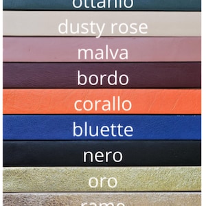 May include: A color chart with 11 leather swatches, each labeled with an Italian word for a color. The colors are: cuoio (brown), ottanio (teal), dusty rose (pink), malva (purple), bordo (burgundy), corallo (orange), bluette (blue), nero (black), oro (gold), rame (copper), and rosso (red).
