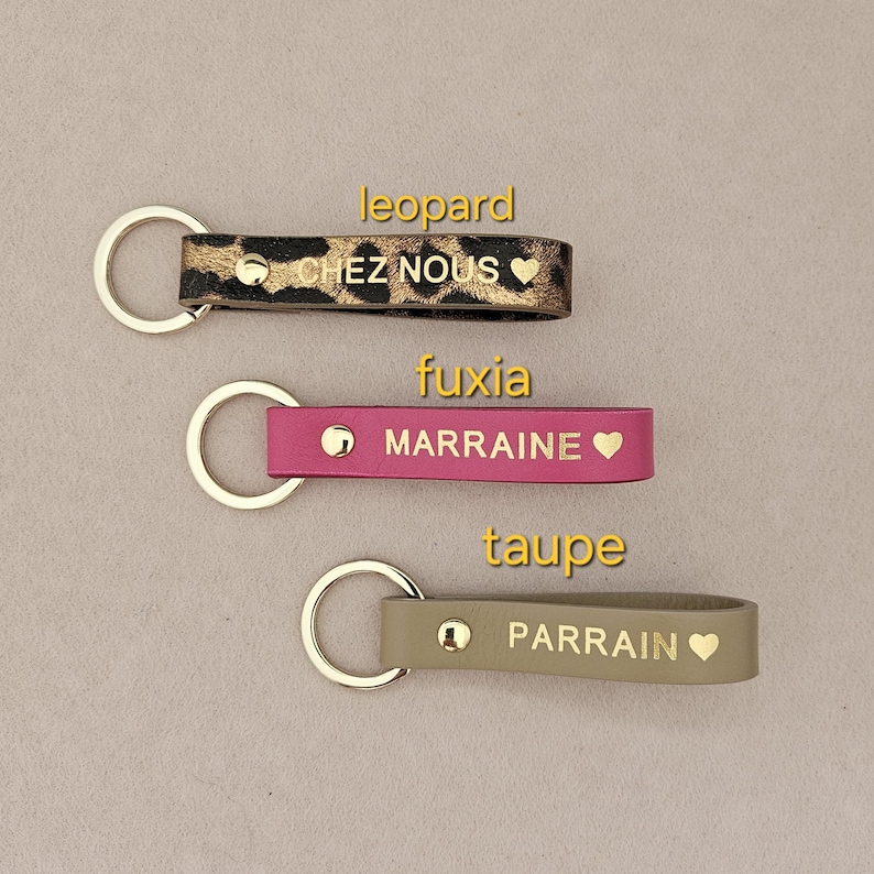 May include: Three leather keychains with gold lettering and a heart symbol. The keychains are in leopard print, fuchsia, and taupe.
