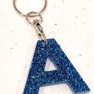 May include: A blue glitter letter A keychain with a silver key ring and clasp.