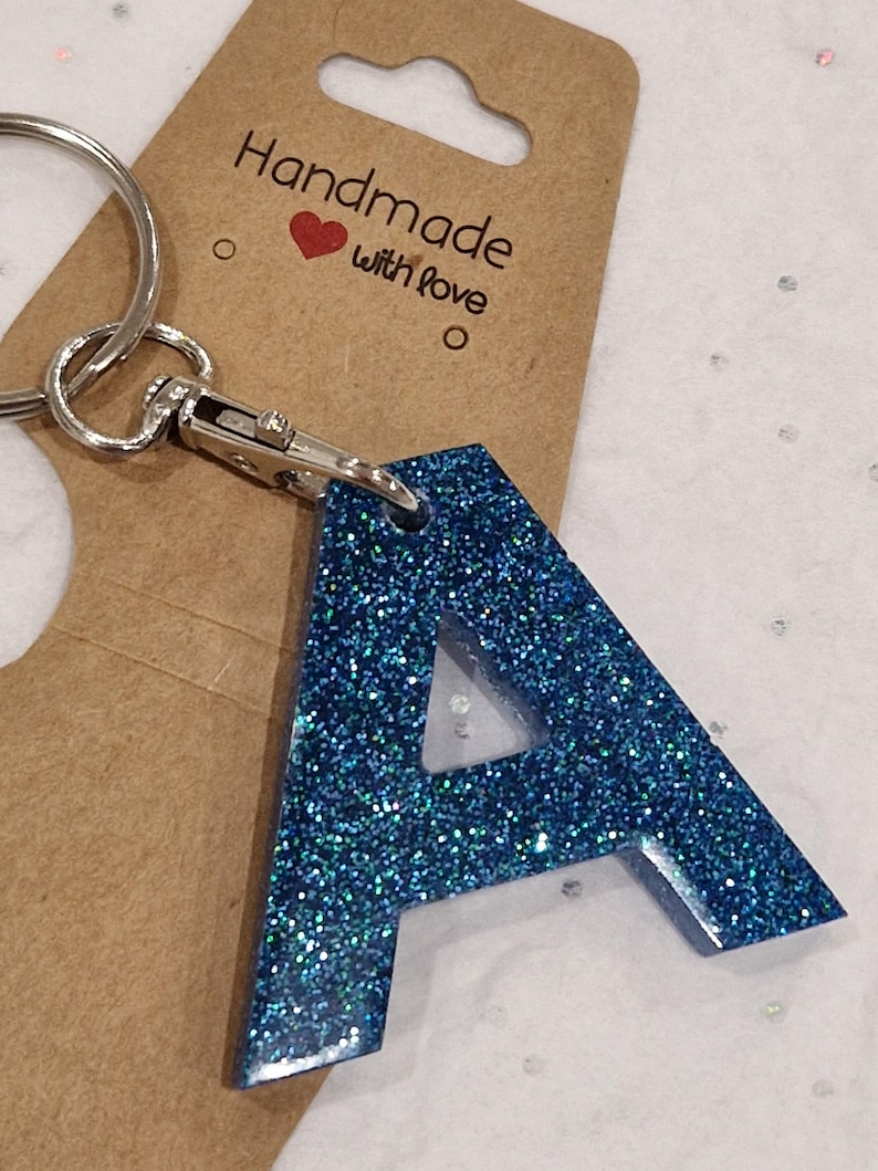 May include: A blue glitter letter A keychain with a silver ring and clasp. The keychain is attached to a brown card with the text "Handmade with love".