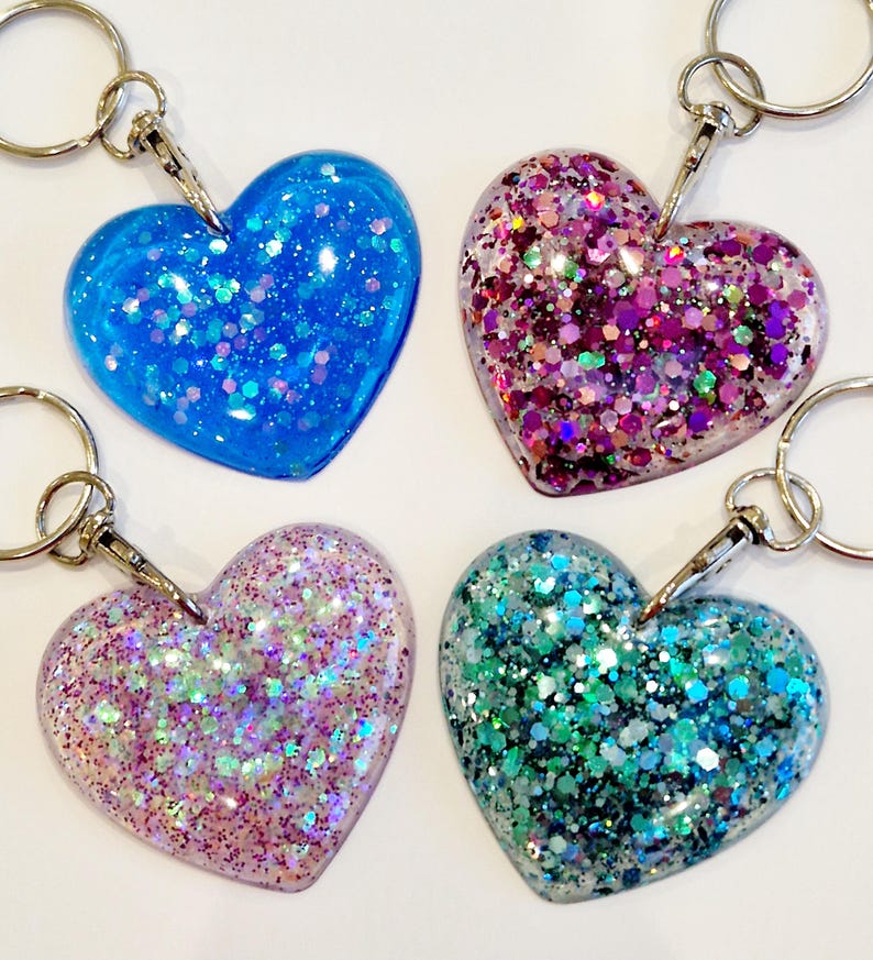May include: Four heart-shaped keychains with glitter embedded in clear resin. The keychains are blue, pink, purple, and green.
