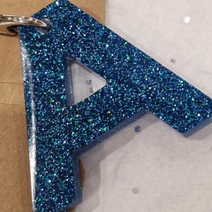 May include: A blue glitter resin keychain shaped like the letter A.