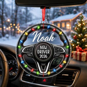 May include: A circular car ornament featuring a black steering wheel design wrapped in colorful Christmas lights. The center displays the text 'NEW DRIVER 2026' and the name 'Noah' is printed in white script above the wheel, all suspended by a red ribbon.