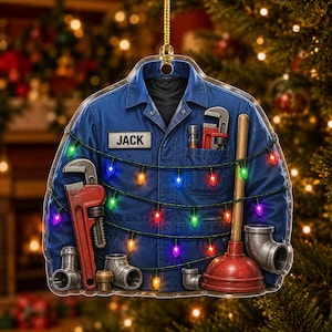 May include: A blue work shirt ornament featuring the name JACK on a white name tag. The shirt is decorated with a string of colorful Christmas lights and various plumbing tools, including a large red pipe wrench and a red rubber plunger.