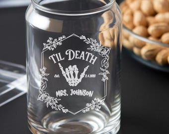 May include: A clear glass can with a white design that says "Til Death Est. 2.4.2023 Mrs. Johnson" with a skeleton hand making a shaka sign.