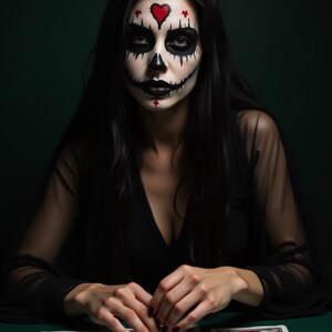 May include: A person with Day of the Dead-style face paint, including a heart on the forehead and black accents around the eyes and mouth. The person is wearing a black dress and is seated at a green table with tarot cards.