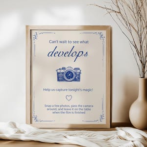 May include: A framed sign with a vintage camera illustration and the text "Can't wait to see what develops. Help us capture tonight's magic! Snap a few photos, pass the camera around, and leave it on the table when the film is finished."