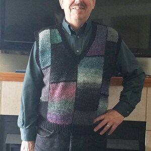 May include: A man wearing a black button-down shirt with a multi-colored knitted vest. The vest has a patchwork design with squares of green, blue, purple, and black.
