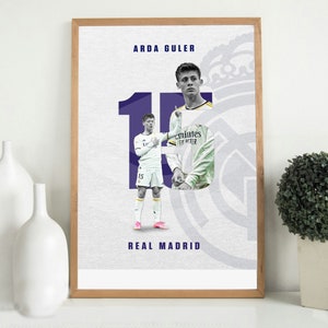 May include: A framed poster featuring Arda Guler in a Real Madrid uniform. The poster has a white background with a large number 10 in purple, and the Real Madrid logo. The player's name and team name are also displayed.