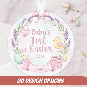 May include: A round, white ornament with a pink and lavender floral wreath, a baby bunny, a yellow chick, and the text "Baby's First Easter 2025 Liam".