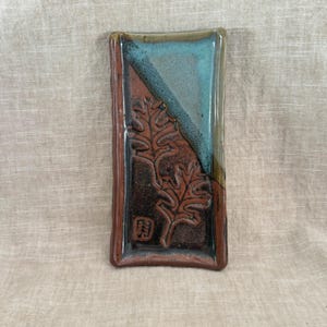 May include: Rectangular ceramic dish with a brown, teal, and black color scheme. The dish features a diagonal teal section and a brown section with embossed leaf designs. The edges are a darker brown.