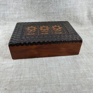 May include: A rectangular wooden box with a dark brown finish. The lid features three carved sunflower designs in a lighter wood tone, surrounded by intricate floral carvings. The box is a decorative storage item.