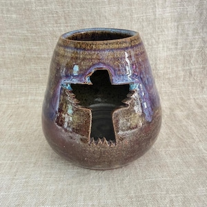 Peut inclure: Un vase en céramique fait à la main avec une découpe en forme de croix. Le vase présente un mélange d'émail marron, violet et bleu, créant un aspect texturé et artistique. L'ouverture en haut mesure environ 10 cm de diamètre.