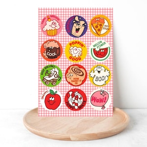 Puede incluir: Una hoja de pegatinas coloridas de estilo retro con varios diseños y texto, incluyendo una magdalena, una pizza y una rodaja de sandía. Las pegatinas están dispuestas sobre un fondo a cuadros rosa y blanco.