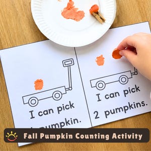 Może przedstawiać: Arkusz aktywności do druku z dwoma czarno-białymi rysunkami liniowymi wózków z tekstem I can pick 1 pumpkin oraz I can pick 2 pumpkins. Pomarańczowe plamy farby przedstawiają dynie, obok znajduje się biały papierowy talerzyk z farbą.