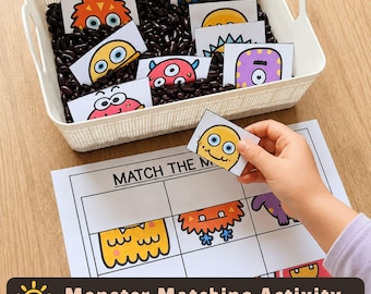May include: A white plastic basket filled with black beans and several small rectangular cards featuring colorful cartoon monster illustrations. A matching activity sheet with the text MATCH THE M is placed below the basket.