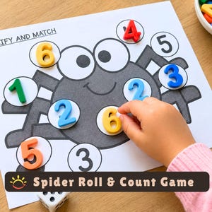 May include: A Spider Roll & Count game sheet featuring a gray spider illustration with white circles for number placement. The sheet includes colorful plastic numbers 1 through 6 placed on the spider, with the text IDENTIFY AND MATCH visible.