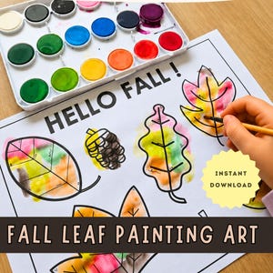 Op de afbeelding: Een wit vel papier met zwarte contouren van bladeren en een dennenappel, met de tekst HELLO FALL! en een gele ster met INSTANT DOWNLOAD. Een aquarelverfset met twaalf kleuren ligt boven het papier, samen met een penseel.