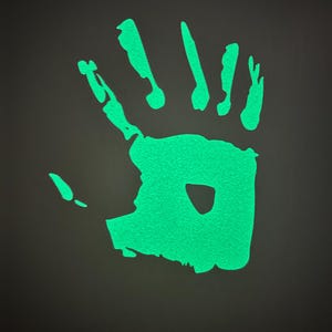 Könnte beinhalten: Ein leuchtend grüner Handabdruck auf einem dunkelgrauen Hintergrund. Der Handabdruck ist eine Silhouette einer Hand mit fünf Fingern.