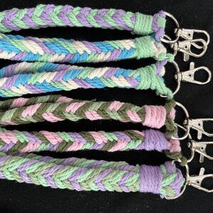 May include: A selection of braided rope keychains in pastel shades of lavender, blue, green, and pink. Each keychain features a silver-coloured clasp for attaching keys. The keychains are made from thick, woven rope.