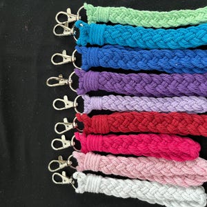 May include: A selection of braided wrist lanyards in a range of colours: green, teal, blue, purple, lavender, red, pink, light pink, and white. Each lanyard is fitted with a silver-coloured swivel clasp for attaching keys or other items.