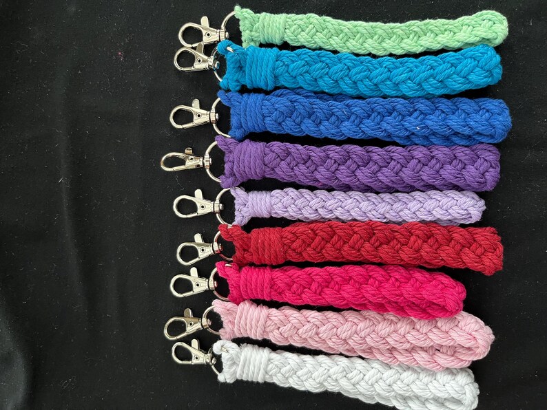 May include: A selection of braided wrist lanyards in a range of colours: green, teal, blue, purple, lavender, red, pink, light pink, and white. Each lanyard is fitted with a silver-coloured swivel clasp for attaching keys or other items.