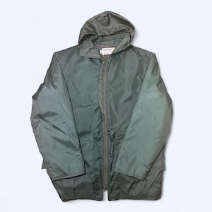 May include: A green hooded jacket with a full-length zipper and two front pockets. The jacket has a simple design and a relaxed fit. The hood is attached and the jacket is made of a lightweight material. The tag reads "CAPTAIN".