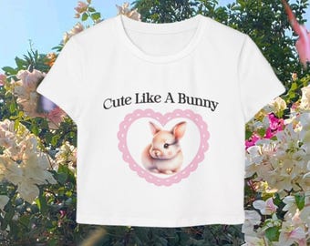 May include: White crop top with short sleeves featuring a pink heart with a cartoon bunny inside and the text "Cute Like A Bunny".