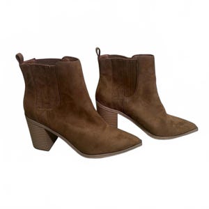 May include: A pair of brown suede ankle boots with pointed toes and stacked block heels. The boots have a pull tab at the back and elastic side panels. The heels are approximately 3 inches high.