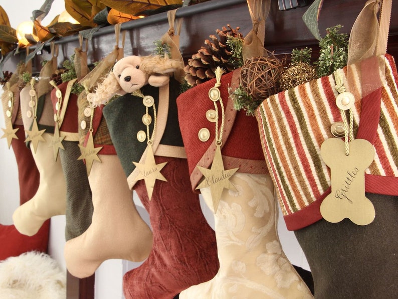 Seven coordinating yet unique Christmas stockings are hanging from a stocking rod on a mantel. Each stocking has a star name tag hanging from the top of three buttons on each stocking's cuff.