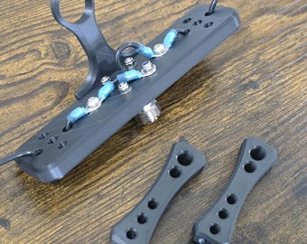 Könnte beinhalten: Ein schwarzes, 3D-gedrucktes Gerät mit Griff und einer Reihe von Löchern, verbunden mit Drähten und kleinen blauen Schläuchen. Zwei passende schwarze Teile mit mehreren Löchern sind ebenfalls vorhanden. Die Artikel befinden sich auf einer Holzoberfläche.