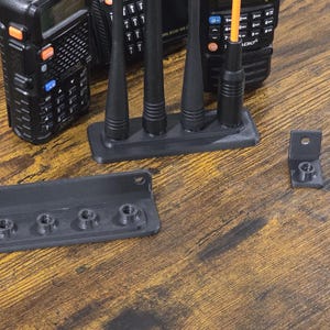 May include: A collection of black communication radio accessories, including antennas and mounting brackets, arranged on a wooden surface. The items are designed for use with two-way radios, offering a practical solution for communication needs.