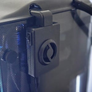 May include: A black computer case with a fan mounted on the side. The fan has a black circular grill with a silver logo in the center. The case has a black power switch on the side.