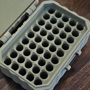 K&ouml;nnte beinhalten: Eine offene, olivgr&uuml;ne Kunststoff-Aufbewahrungsbox mit einem Raster aus kreisf&ouml;rmigen L&ouml;chern. Der Deckel ist ge&ouml;ffnet und gibt das Innere frei. Die Box befindet sich auf einer Holzoberfl&auml;che.