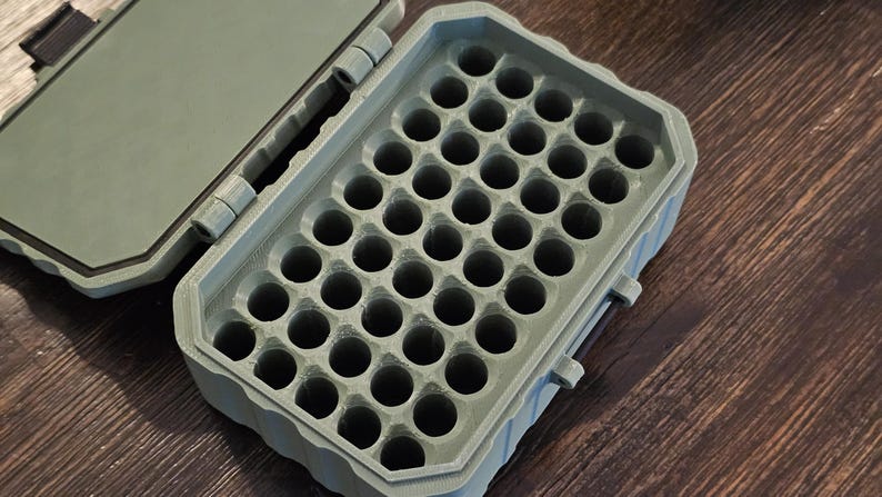 K&ouml;nnte beinhalten: Eine offene, olivgr&uuml;ne Kunststoff-Aufbewahrungsbox mit einem Raster aus kreisf&ouml;rmigen L&ouml;chern. Der Deckel ist ge&ouml;ffnet und gibt das Innere frei. Die Box befindet sich auf einer Holzoberfl&auml;che.