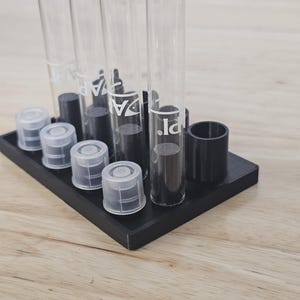 May include: A black plastic test tube rack with six clear glass test tubes. The test tubes have black caps and are labeled with the word "dpl".