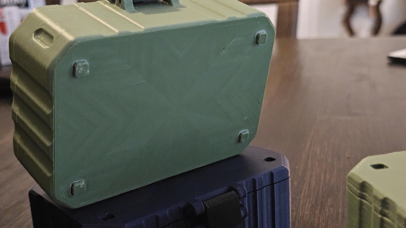 K&ouml;nnte beinhalten: Drei gr&uuml;ne, blaue und beige rechteckige Aufbewahrungsboxen sind auf einer Holzoberfl&auml;che gestapelt. Die Boxen haben einen Griff oben und kleine quadratische F&uuml;&szlig;e unten. Die Boxen haben ein geripptes Design an den Seiten.