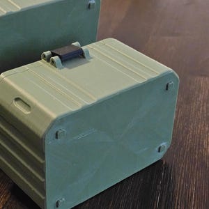 K&ouml;nnte beinhalten: Zwei olivgr&uuml;ne, rechteckige Aufbewahrungsboxen mit abgerundeten Ecken und einem schwarzen Griff. Die Boxen haben ein geriffeltes Design und kleine, quadratische F&uuml;&szlig;e. Eine Box ist auf einer anderen gestapelt.