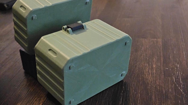 K&ouml;nnte beinhalten: Zwei olivgr&uuml;ne, rechteckige Aufbewahrungsboxen mit abgerundeten Ecken und einem schwarzen Griff. Die Boxen haben ein geriffeltes Design und kleine, quadratische F&uuml;&szlig;e. Eine Box ist auf einer anderen gestapelt.