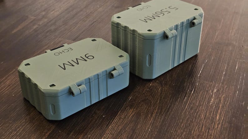 K&ouml;nnte beinhalten: Zwei graue Aufbewahrungsboxen mit Klappdeckeln. Eine ist mit "9MM" und die andere mit "5.56MM" beschriftet. Beide haben das Wort "ECHO" aufgedruckt. Die Beh&auml;lter sind rechteckig und scheinen aus Kunststoff zu sein.