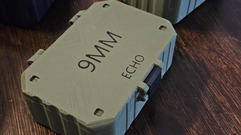 K&ouml;nnte beinhalten: Ein hellgr&uuml;ner rechteckiger Beh&auml;lter mit dem Text "9MM ECHO" in Schwarz aufgedruckt. Der Beh&auml;lter hat einen Klappdeckel und ist mit Riegeln gesichert. Der Hintergrund ist eine dunkle Holzoberfl&auml;che.