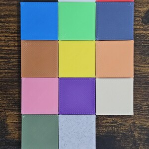 K&ouml;nnte beinhalten: Eine Anordnung von sechzehn kleinen, quadratischen Bl&ouml;cken in Volltonfarben, die in einem Raster angeordnet sind. Die Bl&ouml;cke zeigen eine Vielzahl von Farben, darunter Schwarz, Wei&szlig;, Rot, Blau, Gr&uuml;n und Braun. Die Bl&ouml;cke liegen auf einer Holzoberfl&auml;che.