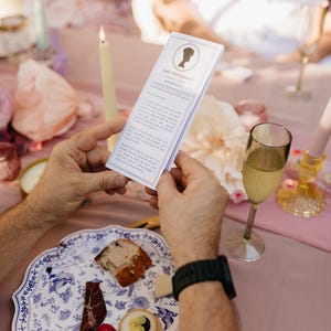 Guest holding a Lady Whistledown printable pamphlet at a garden party table setting with candles, food, and champagne. Perfect for bridal showers, birthdays, or Bridgerton-themed events.