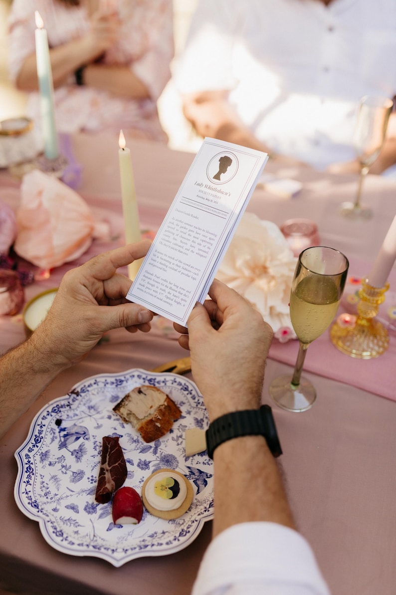 Guest holding a Lady Whistledown printable pamphlet at a garden party table setting with candles, food, and champagne. Perfect for bridal showers, birthdays, or Bridgerton-themed events.