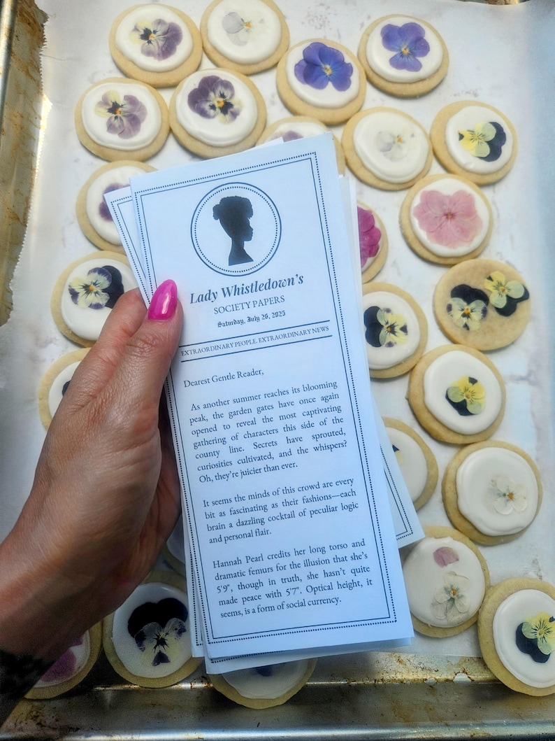 woman with pink nails holding a customizable lady whistledown pamphlet above pressed flower sugar cookies